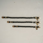 Three black beaded bracelets with gold accents on a light gray background