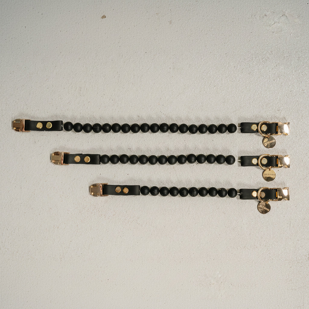 Three black beaded bracelets with gold accents on a light gray background
