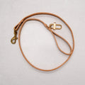 Brown leather dog leash with brass clasp on a light gray background