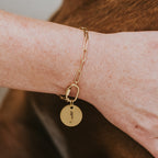 Close-up of a person's hand wearing a gold bracelet with a key charm, petting a brown dog.