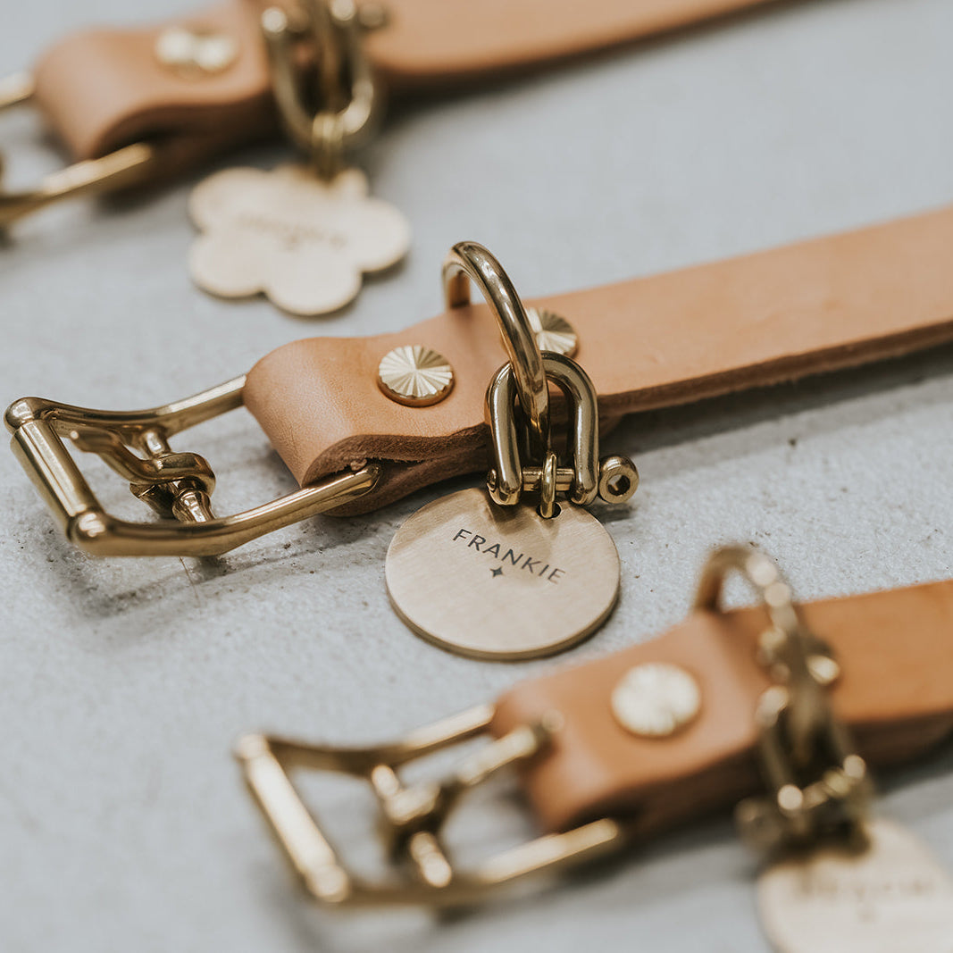 Close-up of leather keychains with gold buckles and name tags on a light gray surface.