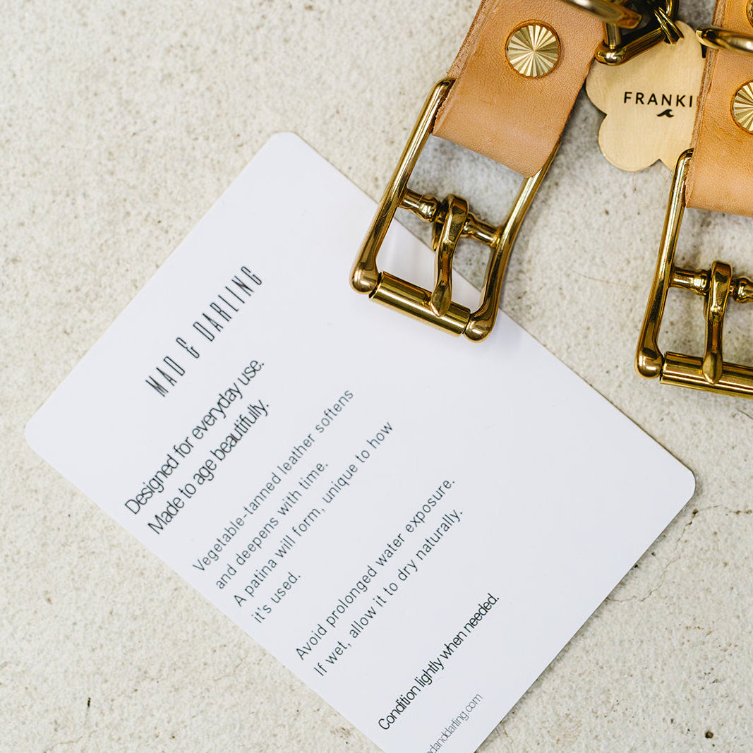 Gold and leather keychain with 'FRANK' tag on a beige background
