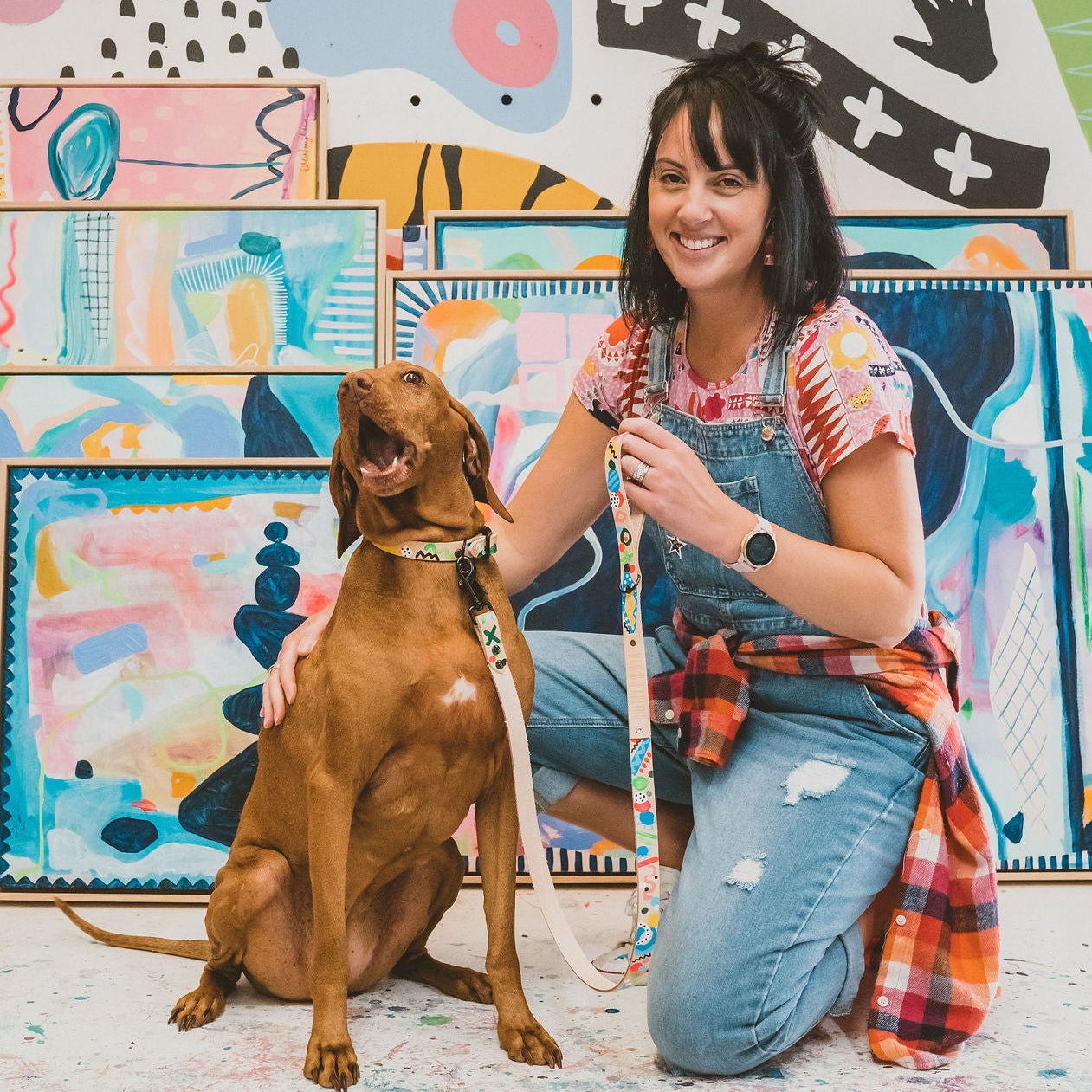 Woman with a dog in front of colorful abstract paintings