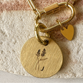 Gold bracelet with a round tag and heart charm on a textured surface